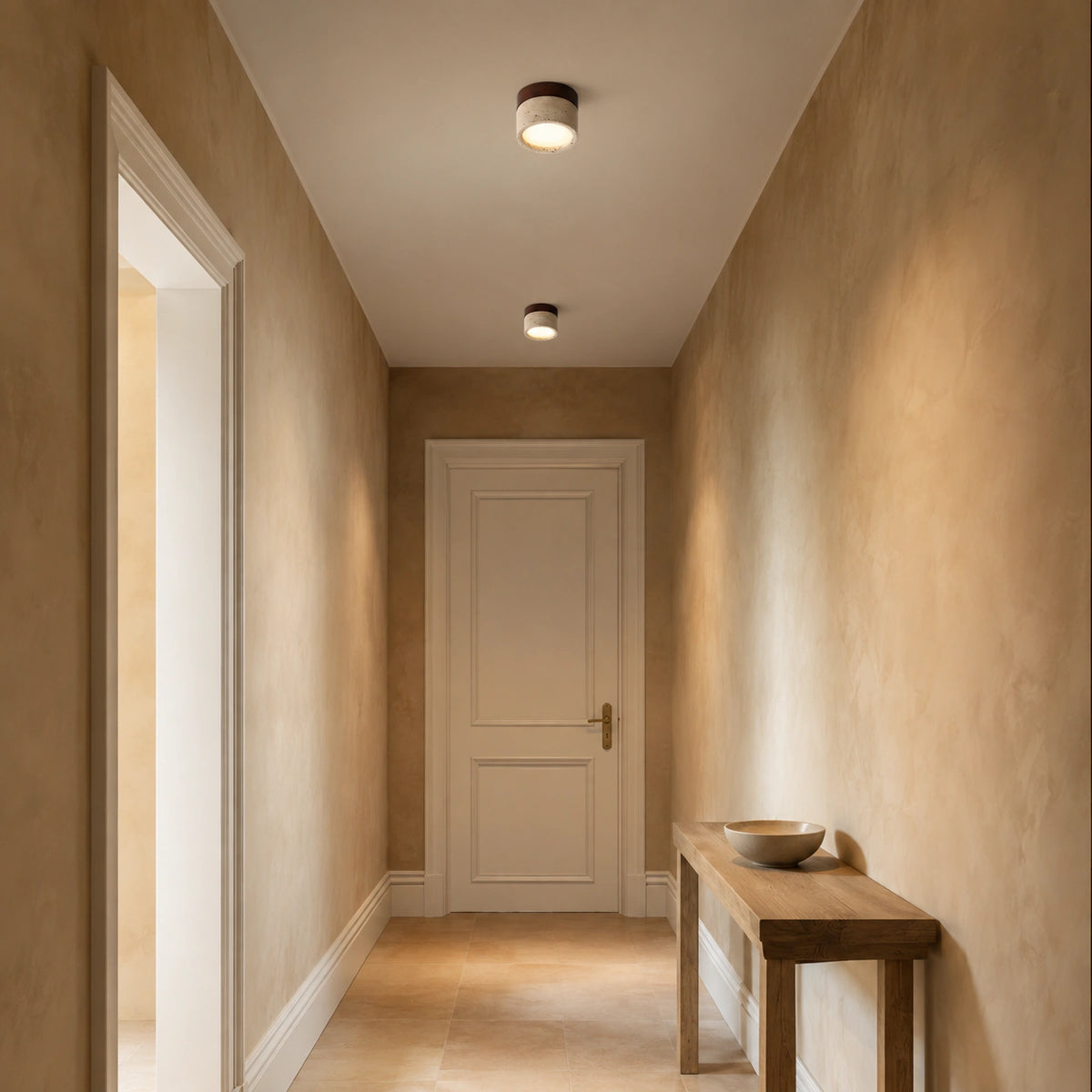 Travertine flush ceiling light with a walnut band lighting a plastered hallway