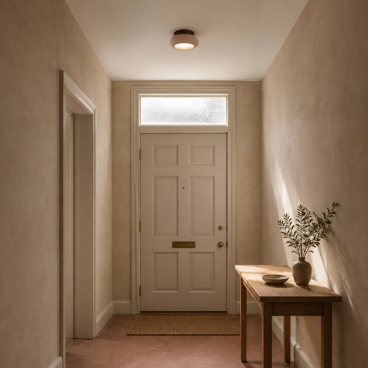Travertine pebble flush ceiling light with a walnut collar lighting a plastered hallway