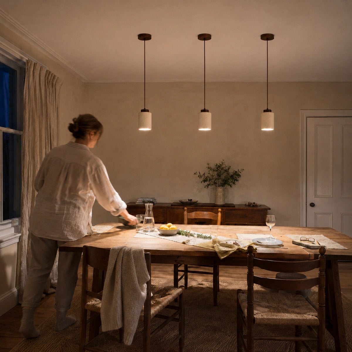 Three travertine cylinder pendant lights hanging above a dining table