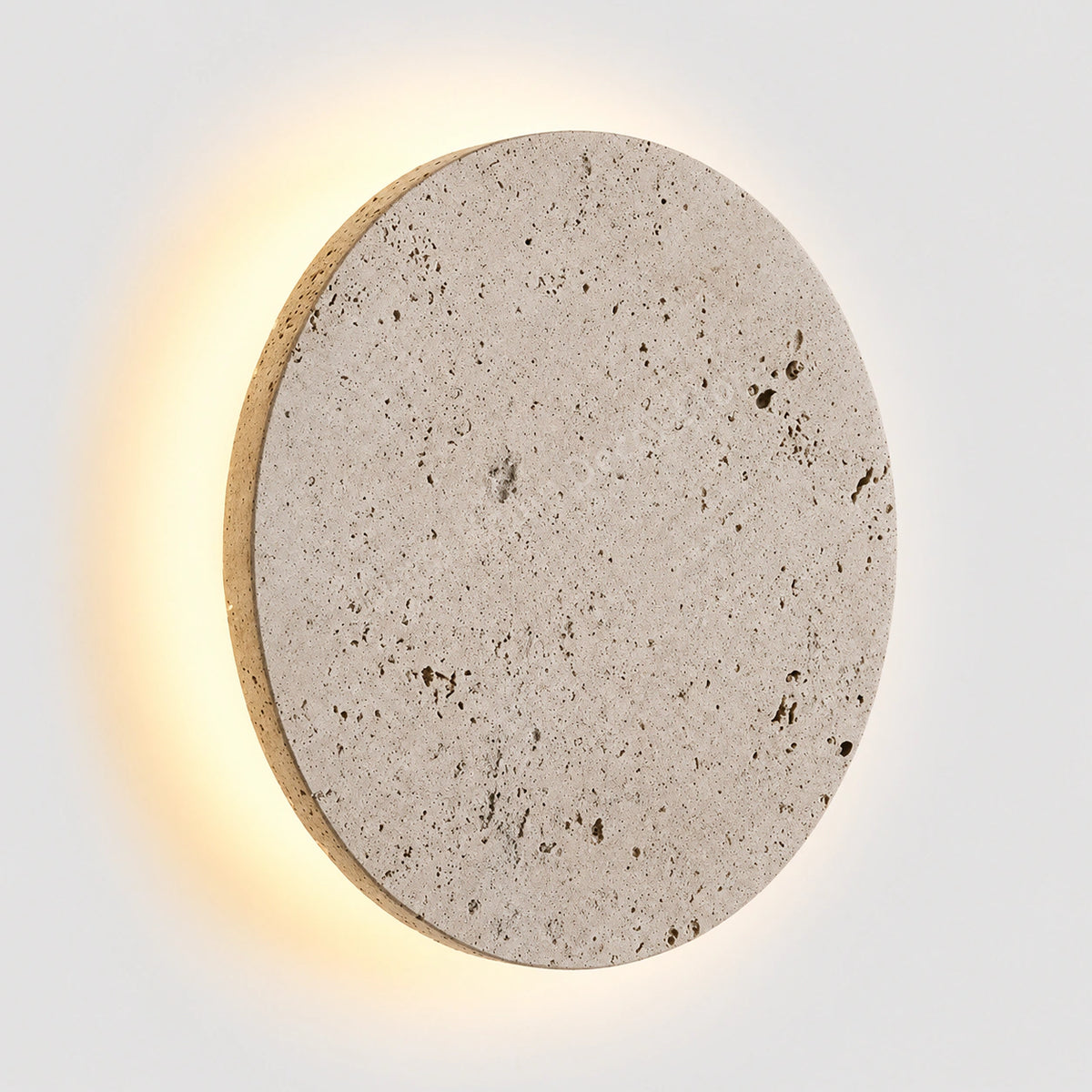 Cream travertine disc wall light floating on a halo of warm light